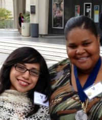 Two girls of color smiling into the camera. Both are wearing badges. One is wearing a medal.